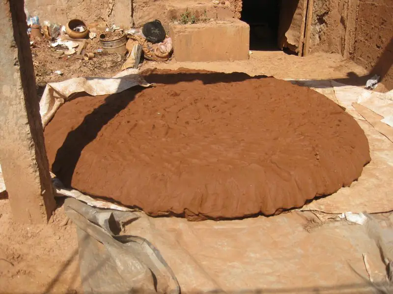 A broad round of worked red clay resting on a tarpaulin in the sun in a pottery workshop.