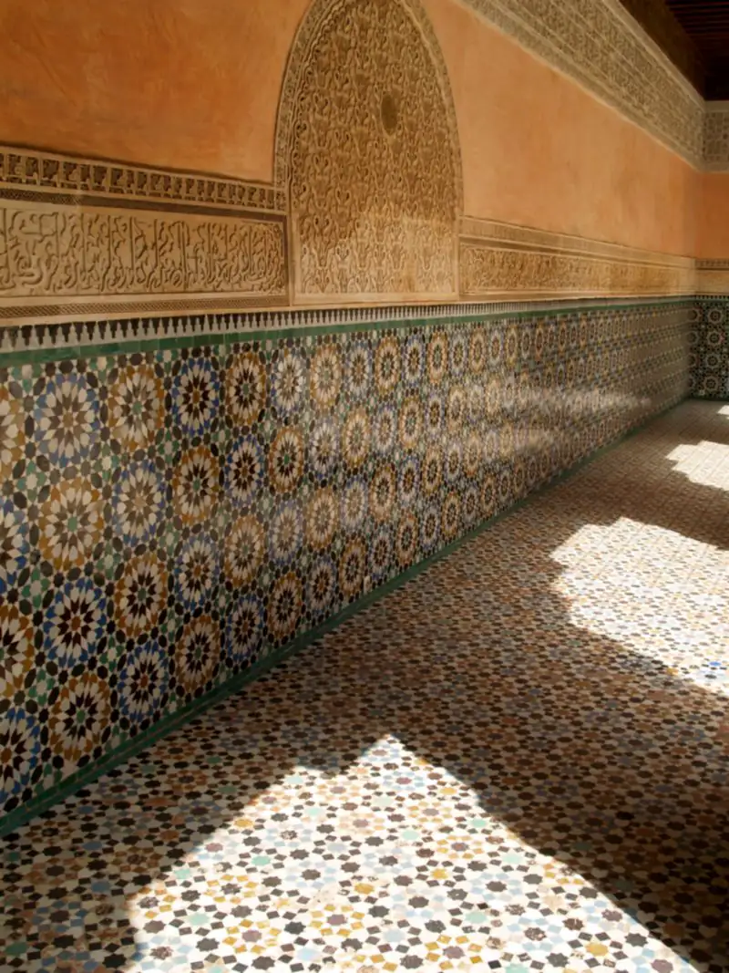 Sunlight falling across a zellige wall and tiled floor in a gallery of the Ben Youssef Madrasa, Marrakech.